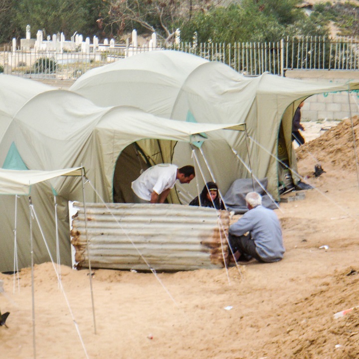 three people cooking behind a corrugated iron windbreak outside their tent in Gaza