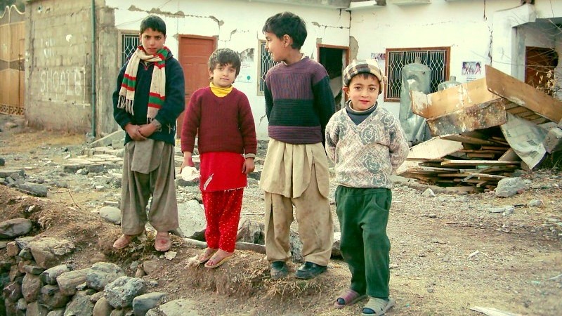 four boys standing on the remains of a wall with destroyed home behind them from PAkistan earthquake 2005