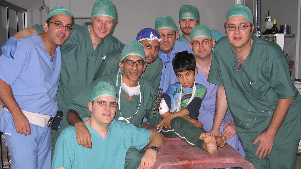 Nine surgical MIST members in scrubs with young boy with arm in external fixator sitting on a theatre table at Rawalpindi eye hospital, in Pakistan 2005